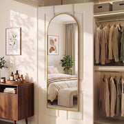 Arched mirror on a door beside a wardrobe with hanging clothes