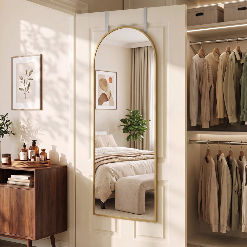 Arched mirror on a door beside a wardrobe with hanging clothes