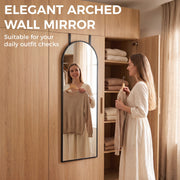 Woman holding a top up while checking her outfit in an arched mirror by a wardrobe