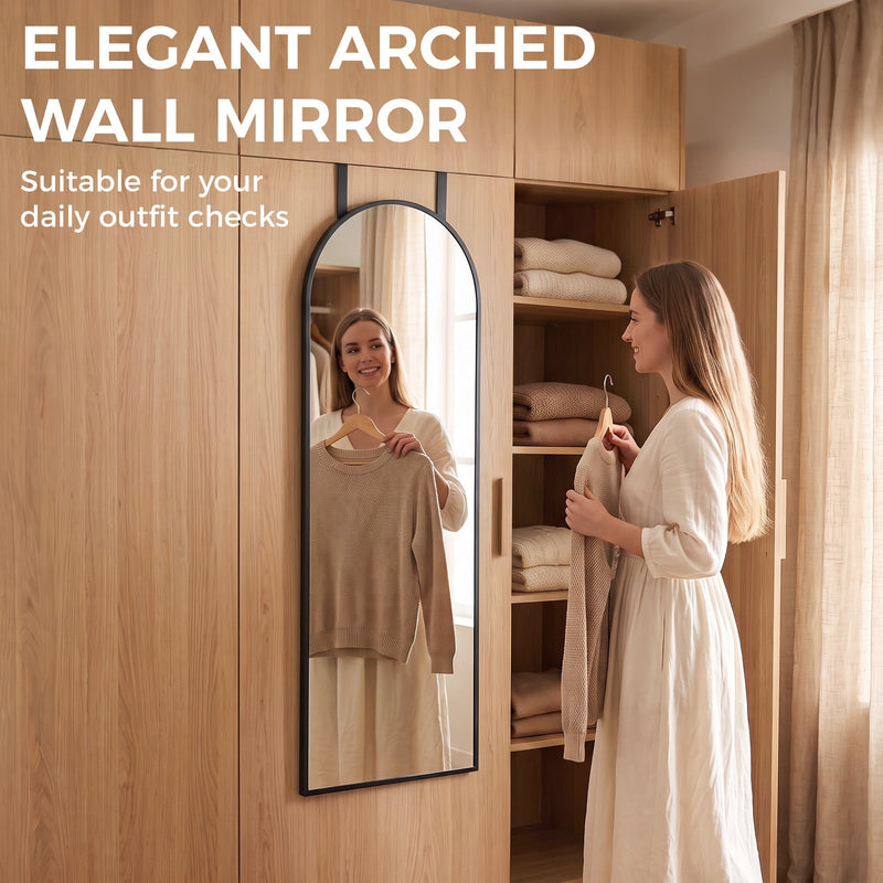 Woman holding a top up while checking her outfit in an arched mirror by a wardrobe