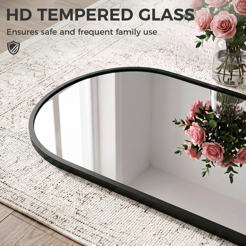 Close-up of the arched mirror frame and tempered glass lying on a rug beside roses