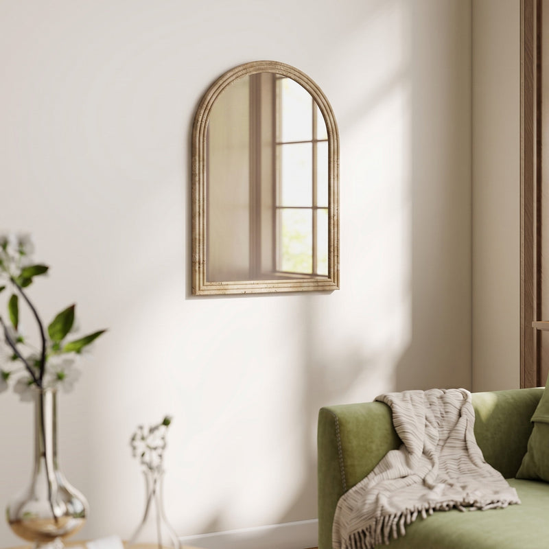 Brown arched mirror mounted above a green sofa in a living room