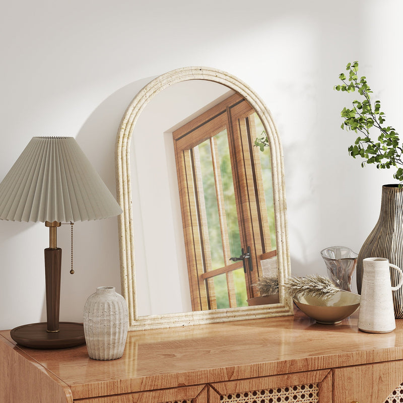 Beige arched mirror leaning on a wooden sideboard beside a table lamp