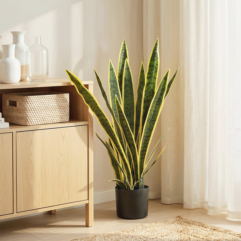 Artificial snake plant beside a wooden cabinet in a bright living room