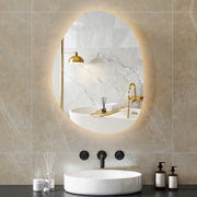 Asymmetric LED bathroom mirror, 70 x 50 cm: warm-lit above a bath in a marble-tiled bathroom
