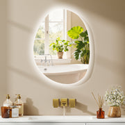 Asymmetric LED bathroom mirror, 70 x 50 cm: backlit above a bath shelf with a window and plants