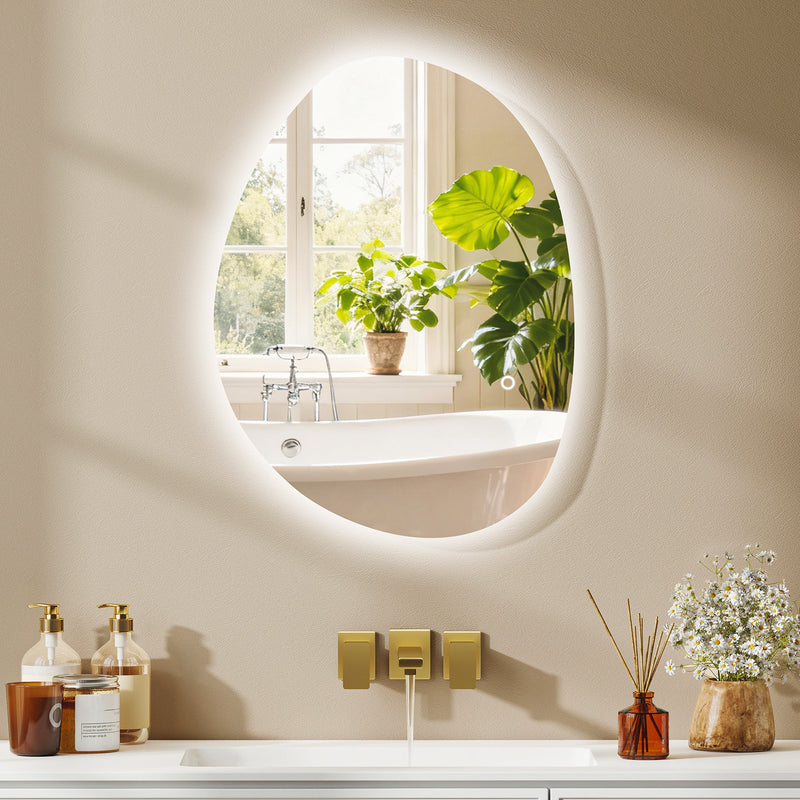 Asymmetric LED bathroom mirror, 70 x 50 cm: backlit above a bath shelf with a window and plants