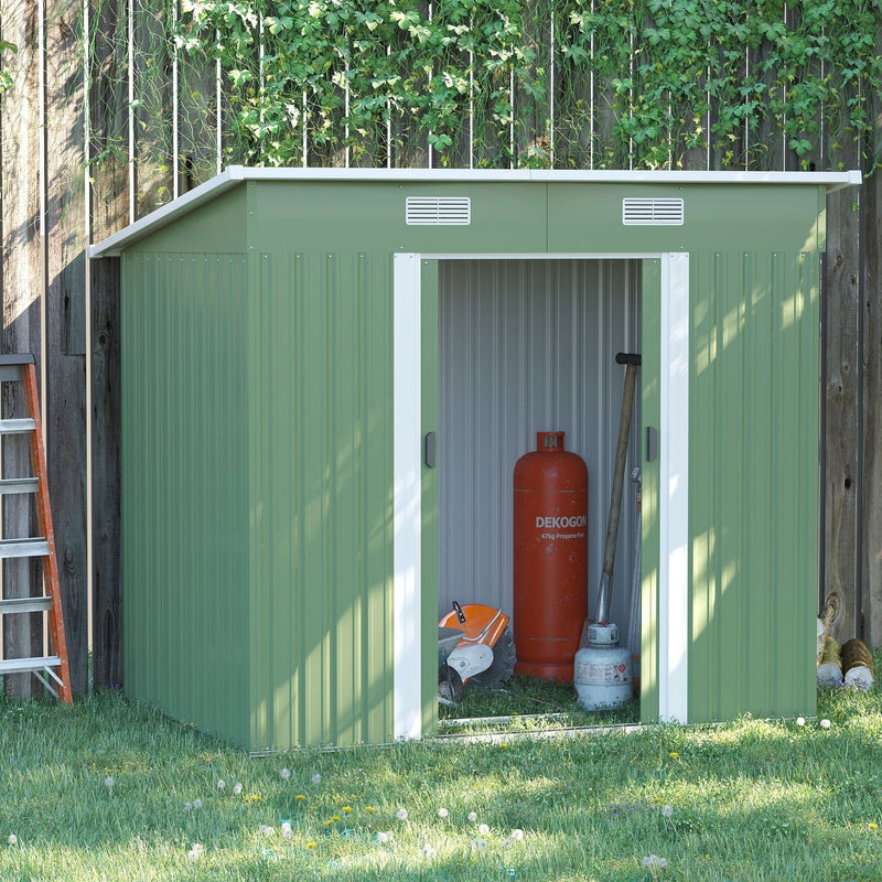 Light green Outsunny 7x4ft metal garden shed against a wooden fence with its sliding doors open on a sunny lawn