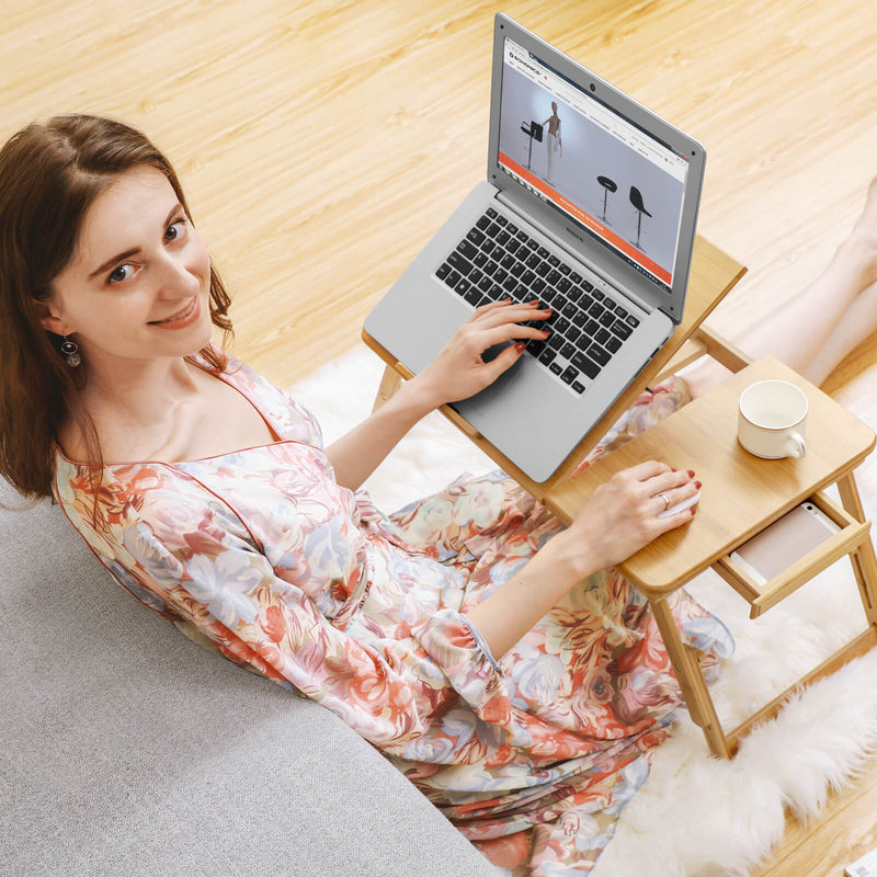Woman sitting on the floor typing on a laptop set on the bamboo table with a mug in the cup recess