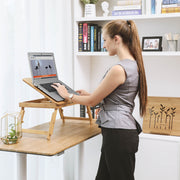 Woman standing at a desk typing on a laptop raised on the bamboo table in front of a bookshelf