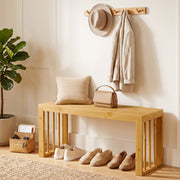 Bamboo bench in a hallway with shoes underneath, a cushion, handbag and coat hooks above