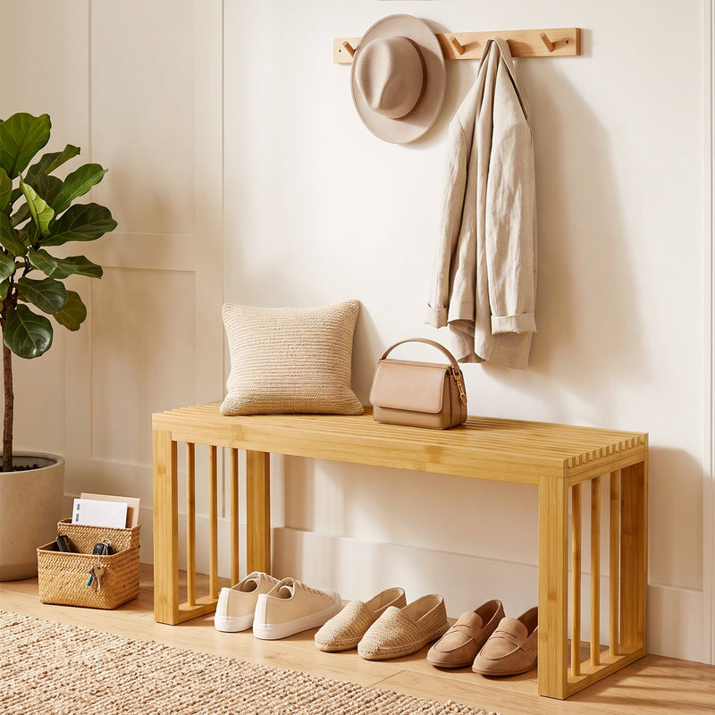Bamboo bench in a hallway with shoes underneath, a cushion, handbag and coat hooks above