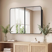 Black mirror cabinet hung above a rattan-front sideboard with plants