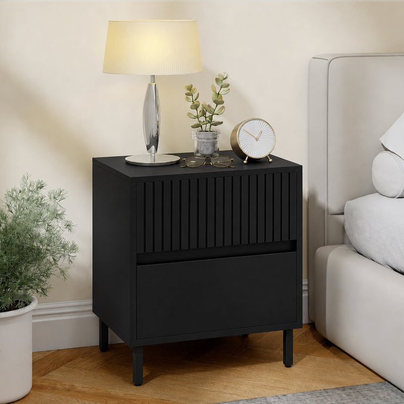 Black bedside cabinet used as a nightstand beside a bed with lamp and decor