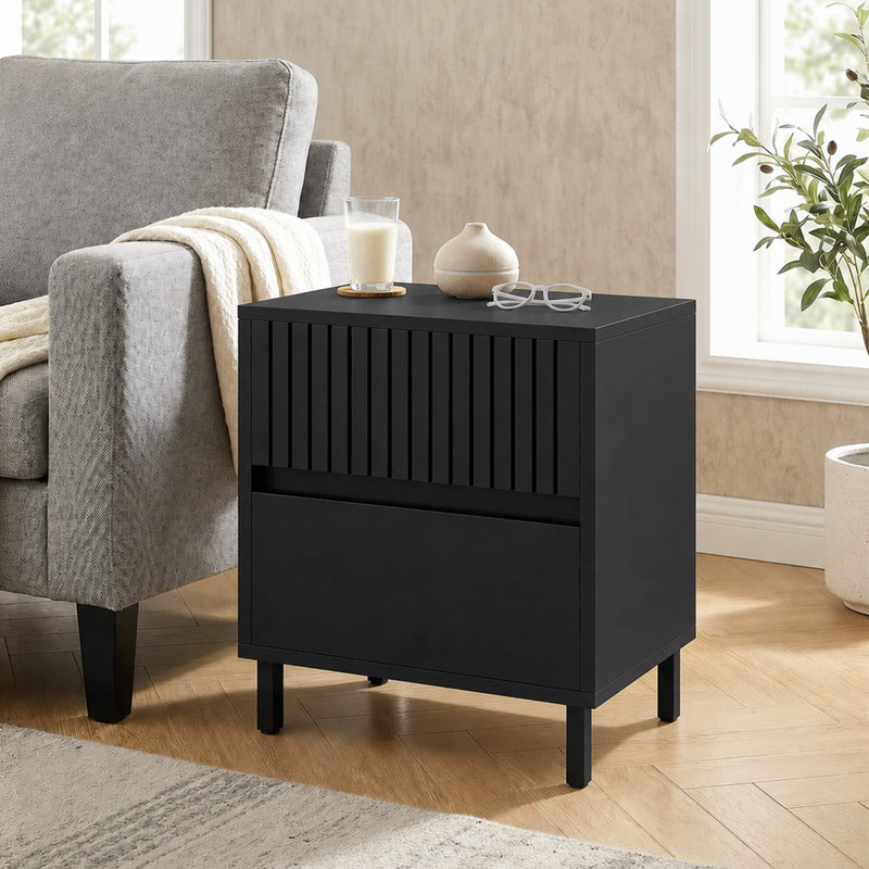 Black bedside cabinet used as a side table next to a grey armchair