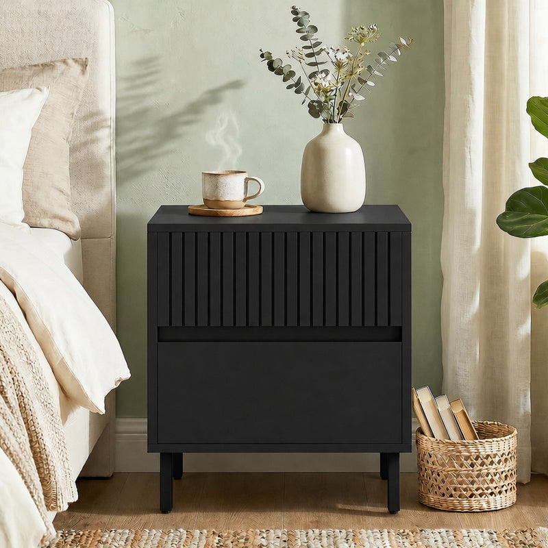Black bedside cabinet in a bedroom setting with a vase and books nearby
