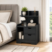 Black bedside table styled next to a bed with a lamp, clock and books on top