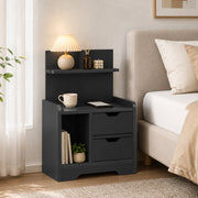 Black bedside table beside a bed with a lit lamp and reed diffuser on top
