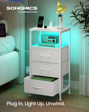 Cloud White bedside table styled beside a bed with turquoise LED light glowing under the open shelf and a phone charging on top