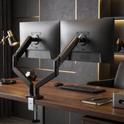 Two monitors on the black dual gas spring arms clamped to a wooden desk