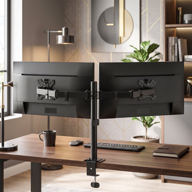 Dual monitor stand holding two screens on a desk with a lamp and shelves behind