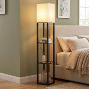 Floor lamp with shelves holding books and a plant next to a bed in a sage green room