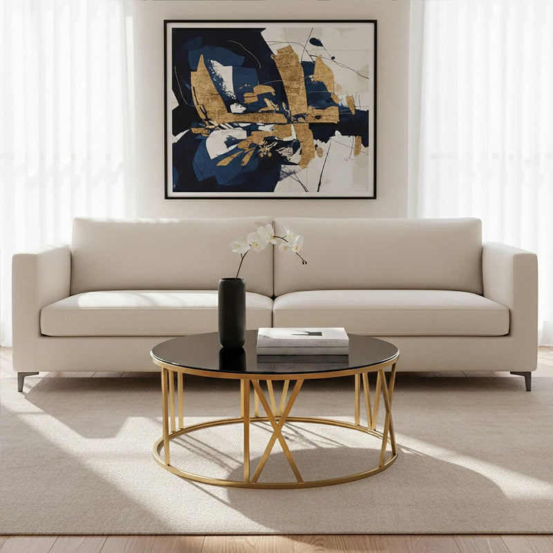 Round gold and black glass coffee table in a living room setting beside a neutral sofa