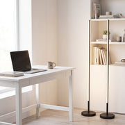 Two black floor lamps beside a white desk and bookshelf