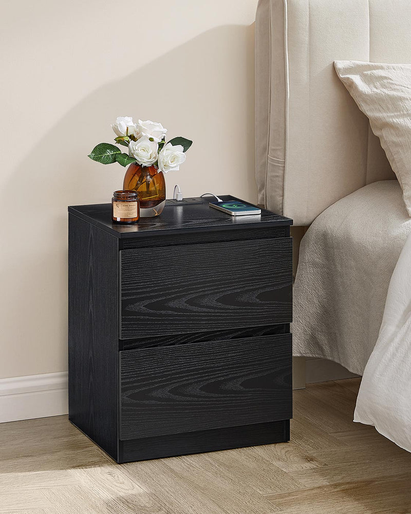 Black nightstand beside a cream upholstered bed with a phone charging on the top panel
