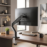 Monitor on the black single arm clamped to a desk beside a window