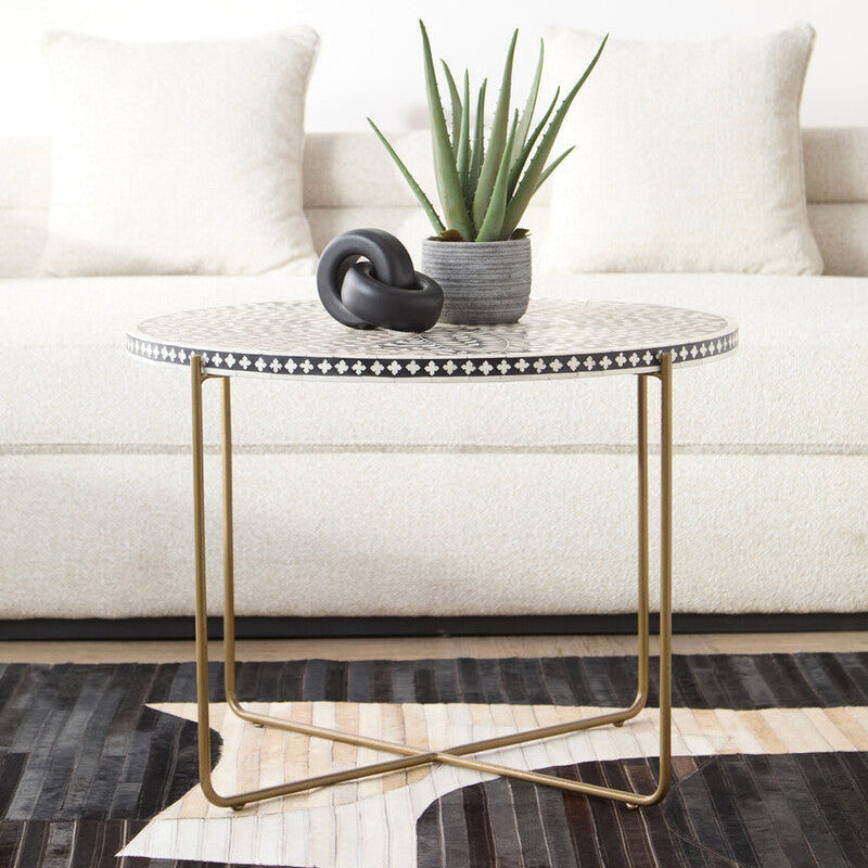 Black and white bone inlay round coffee table with gold cross base in a living room