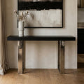 Black wood and glass top console table with silver crossed legs styled in a hallway setting