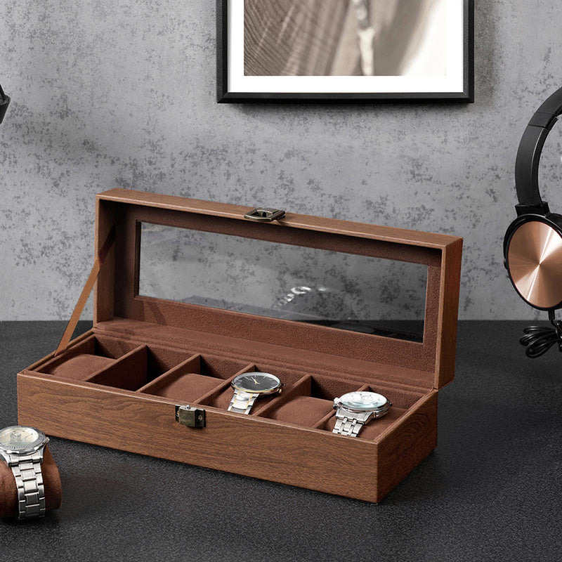 Watch box on a dark desk with one cushion lifted out and a watch beside it
