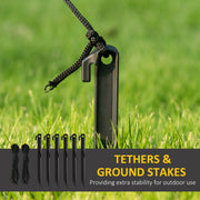 Six ground stakes and two black cords, with a cord clipped to a stake on grass