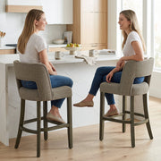 Two women chatting on brown bar stools at a kitchen counter
