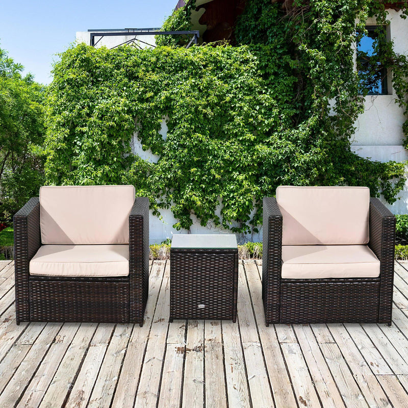Brown rattan bistro set with two armchairs and side table on wooden decking in front of greenery