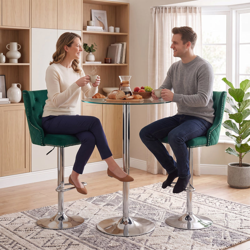 Two people seated on dark green button-tufted bar stools at a round glass bistro table
