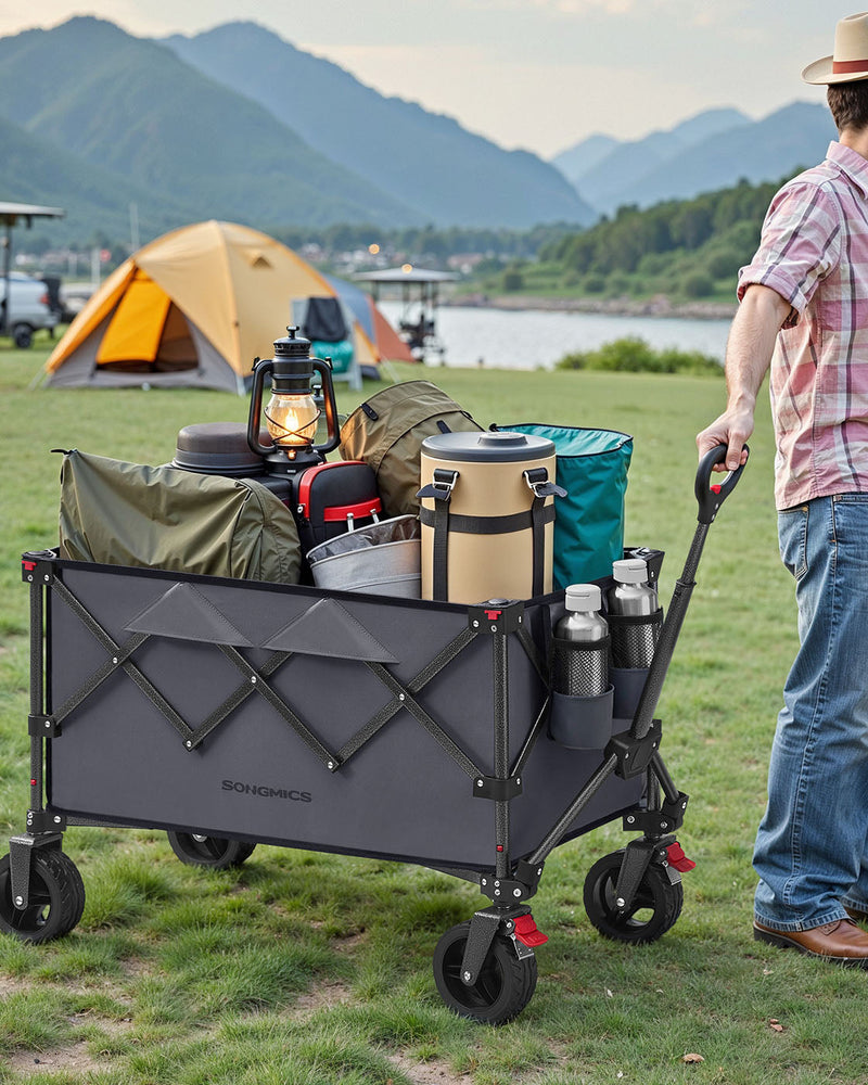 Man pulling the loaded trolley across grass at a lakeside campsite with tents behind