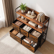 Angled view of the chest of drawers with a plant and books on the shelves and folded clothes in the open drawers