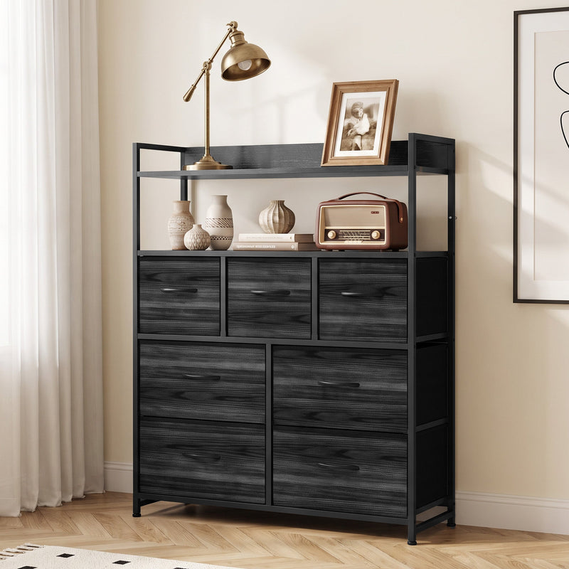 Black 7-drawer chest of drawers in a bedroom with a lamp, framed photo and radio on the shelves