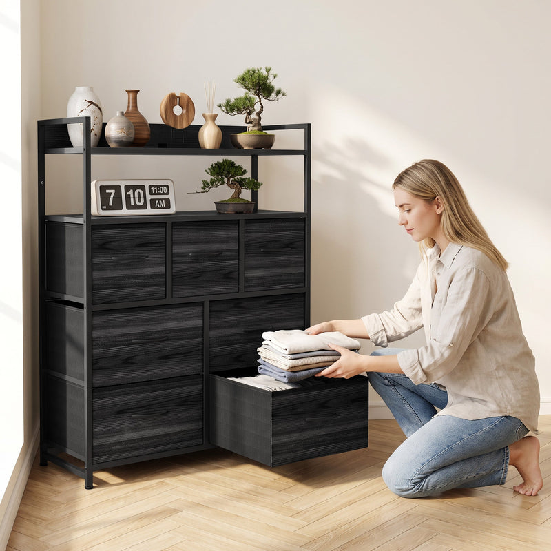 Woman kneeling to fold clothes in a pulled-out fabric drawer of the black chest of drawers