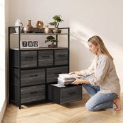 Woman kneeling to fold clothes in a pulled-out fabric drawer of the grey chest of drawers