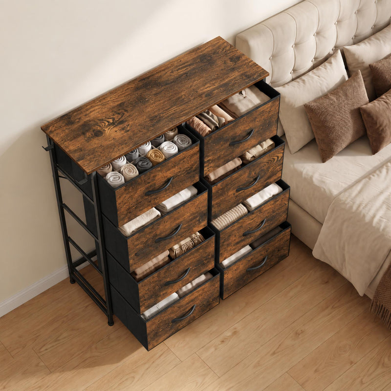 Wood-effect drawers pulled open with folded clothes, beside a bed with cushions