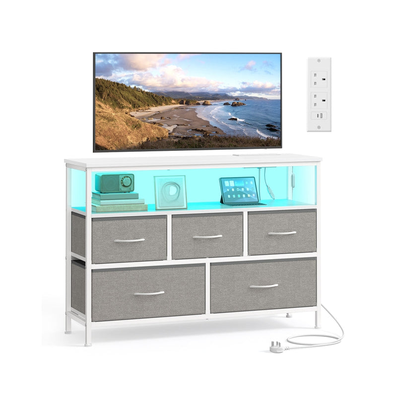 SONGMICS dove grey fabric 5-drawer chest of drawers styled as a TV stand with a wall-mounted TV and power outlet above.
