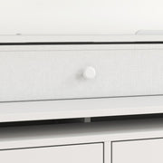 Close-up of a small top drawer with a fabric-look front and round knob in white
