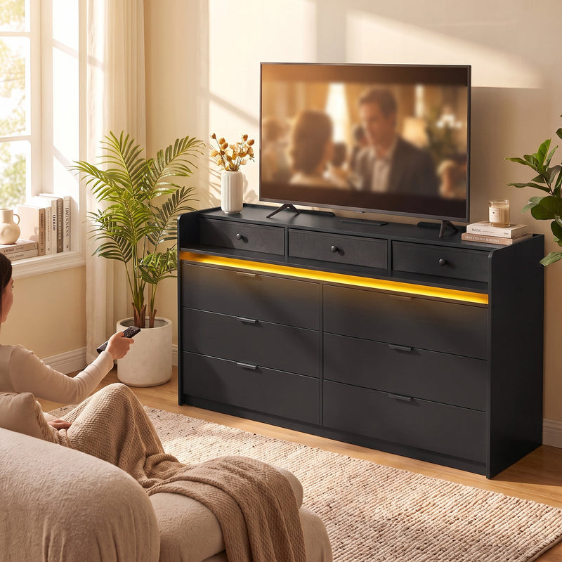 Black chest of drawers under a TV in a living room with a warm LED glow