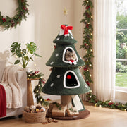 Christmas tree cat tower with a cat in the upper condo beside a plant and wreath