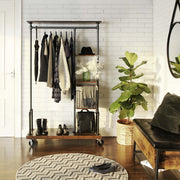 Clothing rack on wheels holding coats and a hat beside a white brick wall and bench