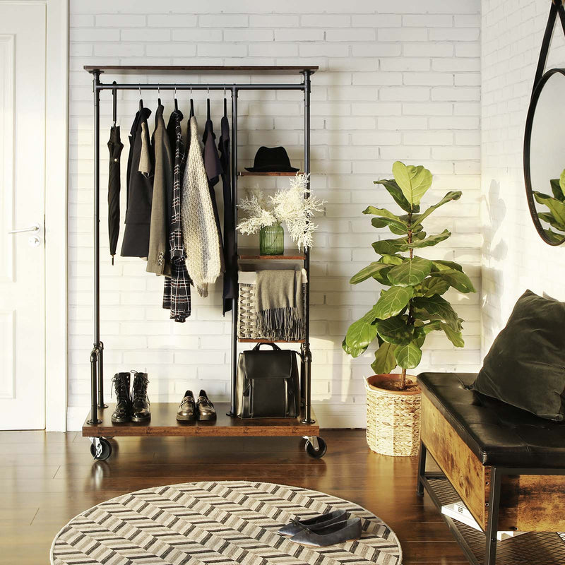 Clothing rack on wheels holding coats and a hat beside a white brick wall and bench