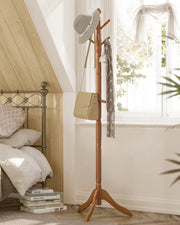 Caramel brown coat rack stand in a bedroom beside a bed holding a hat, bag and scarf